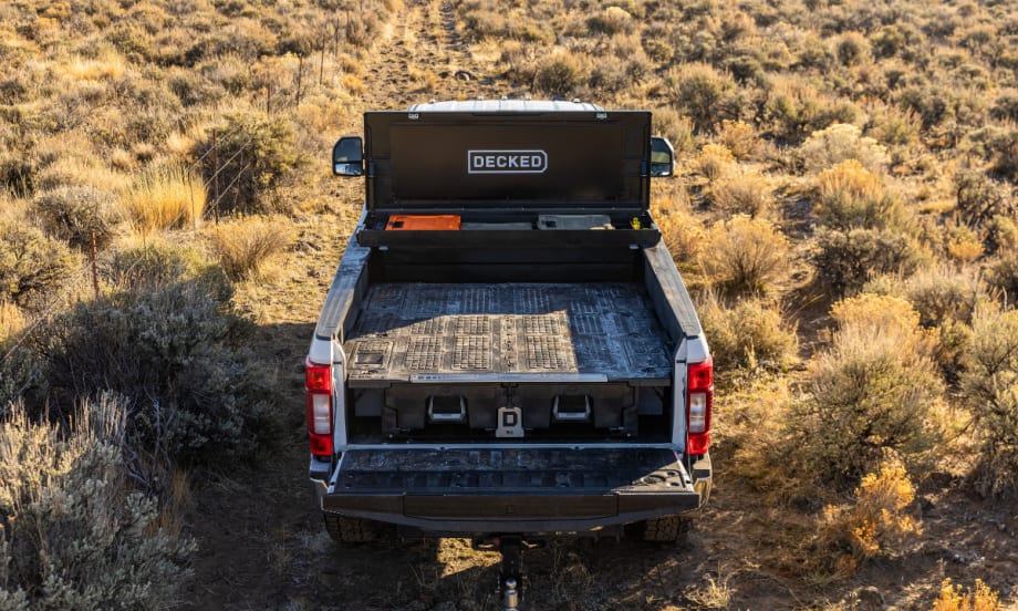 Rear view of a pickup with a DECKED tool box mounted at the front of the open bed in an outdoor setting.
