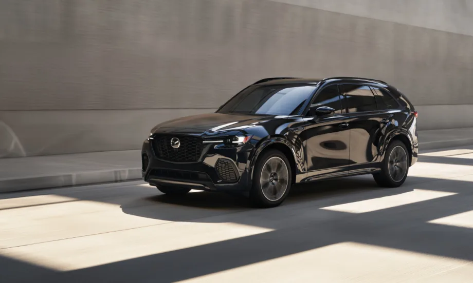 A black Mazda CX-70 crossover driving through an urban roadway with concrete walls in the background.
