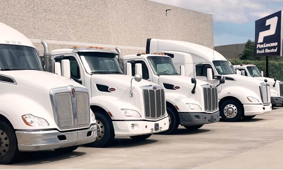 Row of five truck cabs parked outside a building with a PacLease sign in the background.