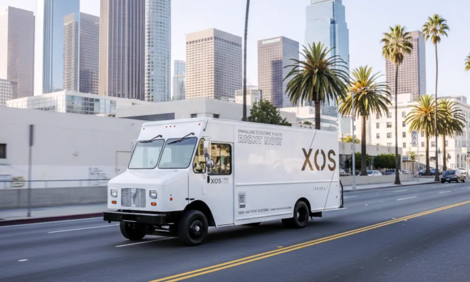 A white step van driving through a downtime area of a large city with tall buildings.