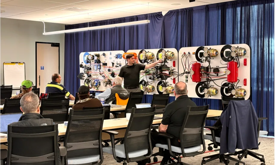 Group in classroom listens as an instructor in front of room demonstrates an air brake system and its components.