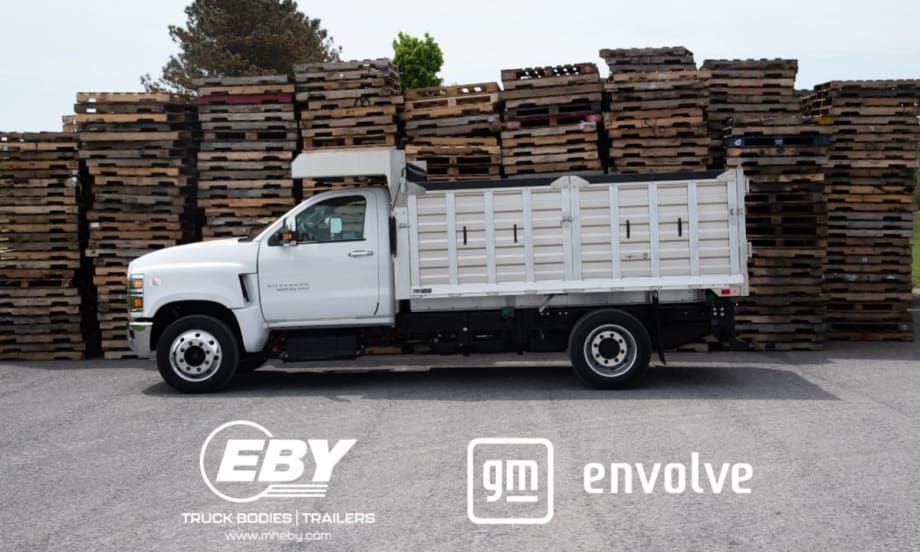 Side view photo of a white stake-bed work truck with logos across the bottom of the image for EBY and GM Envolve.