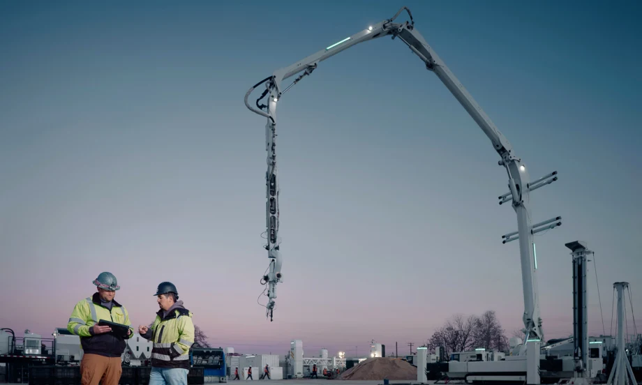 Dark blue sky at dusk, two construction workers, a crane-type structure in the background.