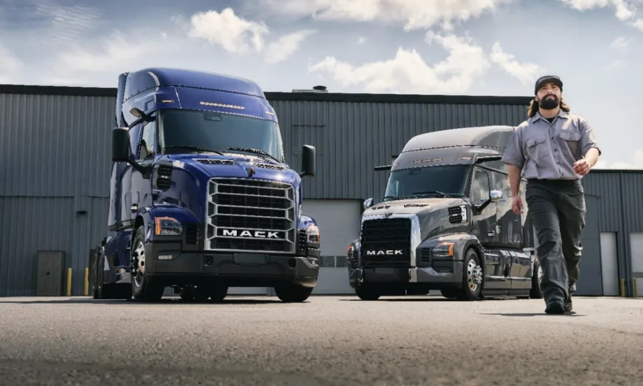 Man walking toward camera with two Mack trucks in the background.
