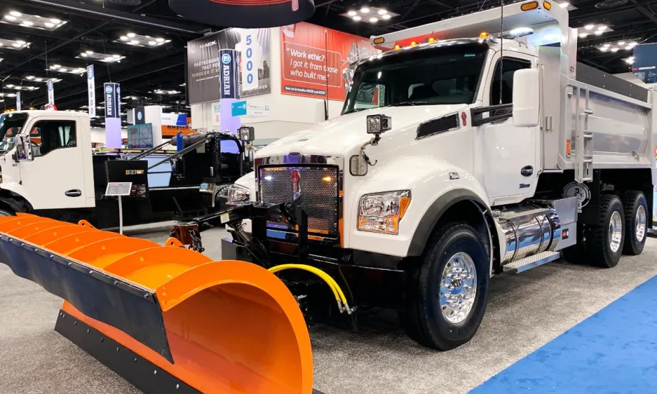 Front angled photo of a white dump truck with an orange snow plow on the front.