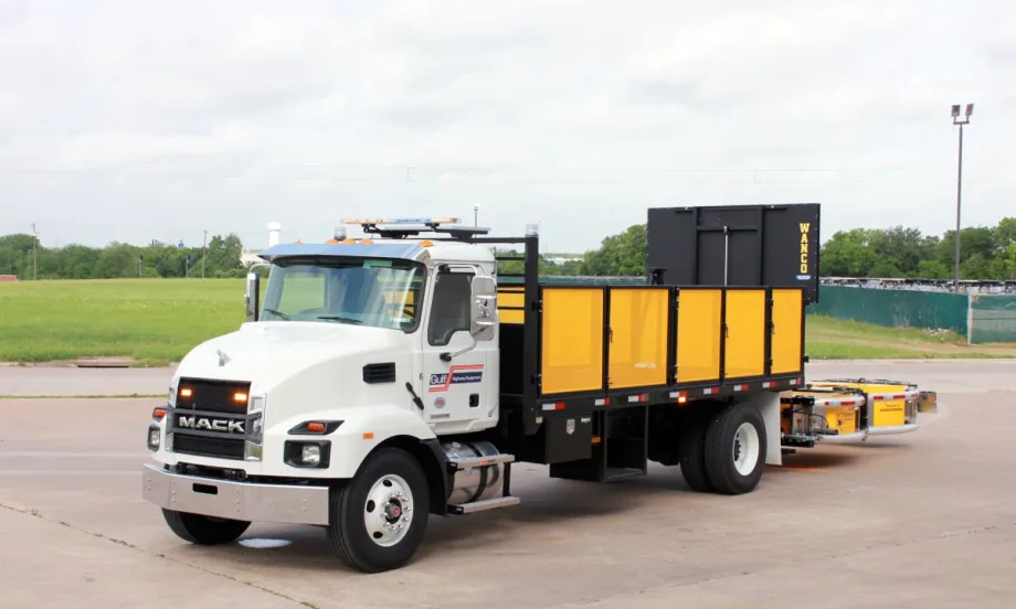 White work truck with yellow bed and yellow rear-mounted crash protection device parked in a parking lot.