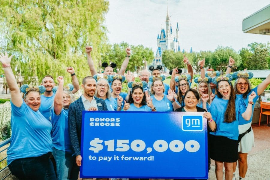 Adults in blue shirts holding a banner with headline $150,000 with Disney World castle in the background.