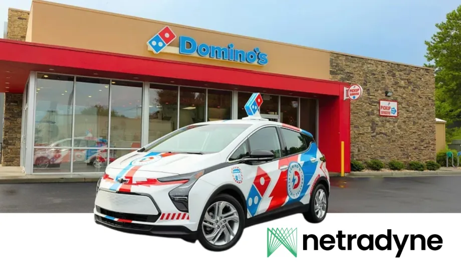 Domino’s-branded electric delivery car parked outside a Domino’s restaurant, featuring red, blue, and white graphics. The image includes the Netradyne logo in the lower corner and storefront pickup signage in the background.