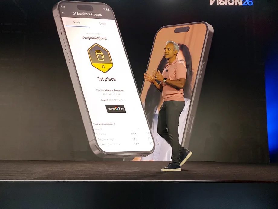 Presenter onstage at Motive Vision 26 conference beside a large smartphone display showing a driver rewards app, highlighting a first-place achievement in a Q1 Excellence Program with points, rankings, and Google Pay integration.