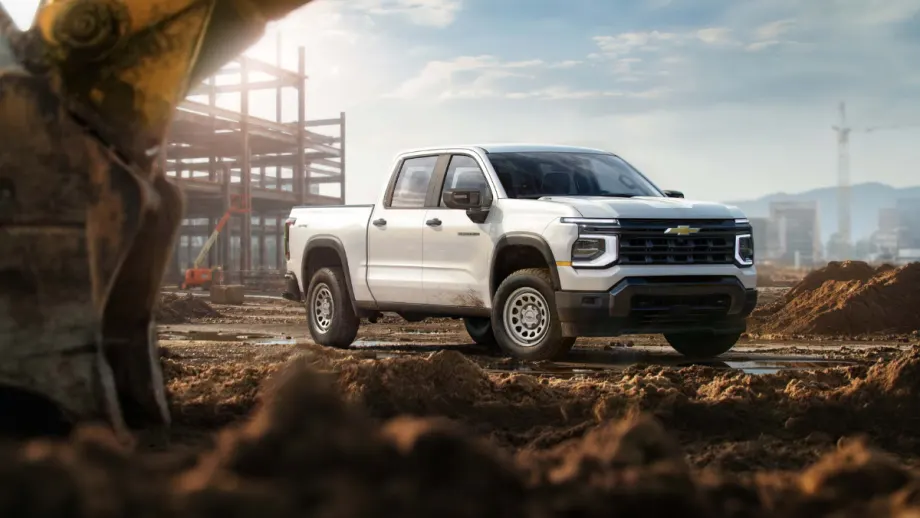 White 2027 Chevrolet Silverado 1500 Work Truck parked at a construction site with steel framing in the background.