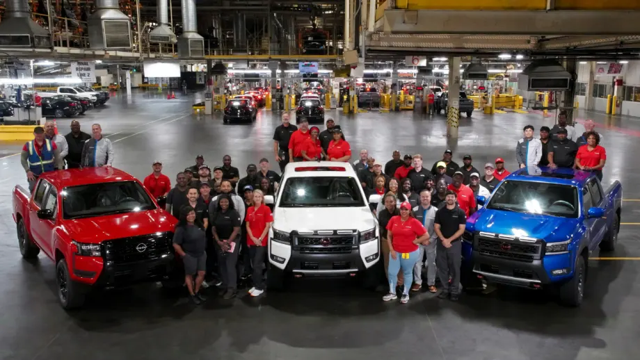 Nissan manufacturing employees gather around red, white, and blue Frontier pickup trucks inside the Canton, Mississippi assembly plant to celebrate a production milestone.