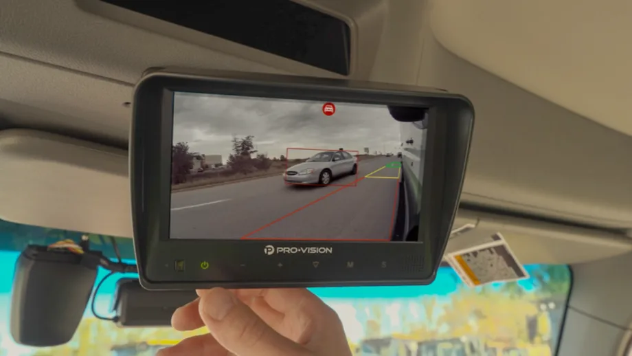 A Pro-Vision monitor mounted inside a commercial vehicle displays a side camera view with AI detection highlighting a nearby passenger vehicle during a lane change.