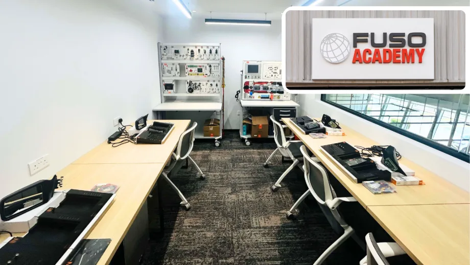 FUSO Academy training classroom featuring workstations, diagnostic equipment, and electronics training benches, with a FUSO Academy logo highlighting the company's technical training facility.