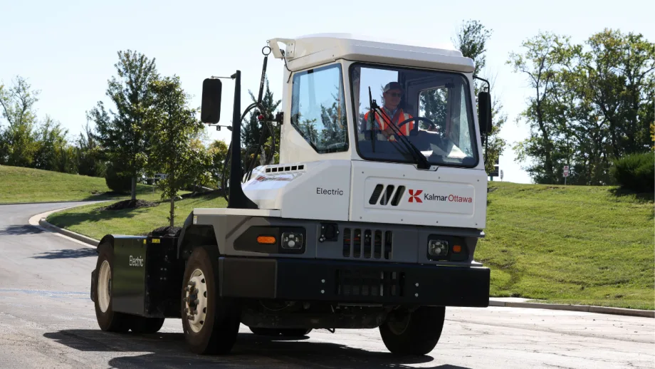 Kalmar Ottawa electric terminal tractor drives on a paved roadway with an operator in the cab, showcasing the zero-emission yard truck in an outdoor commercial fleet setting.