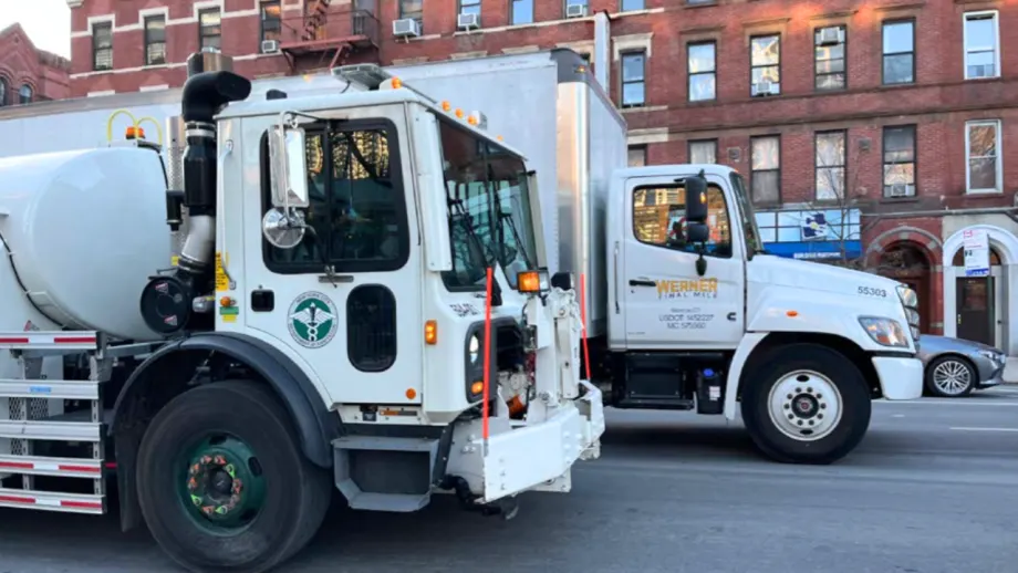 Two commercial trucks, including a municipal service vehicle and a Werner Final Mile truck, parked on a city street in front of brick buildings.