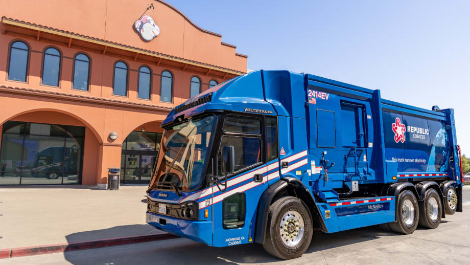 Blue Republic Services McNeilus Volterra ZSL electric refuse truck parked outside a facility, with Republic Services branding and “This truck runs on electricity” displayed on the body.