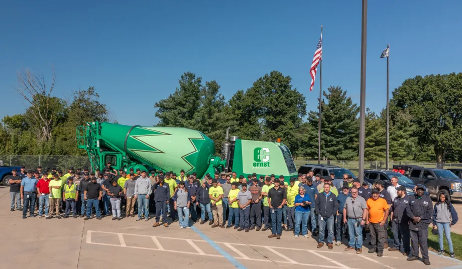 Large group of employees gathered outdoors in front of a green Ernst Concrete mixer truck, posing beneath American and company flags to commemorate a company milestone.