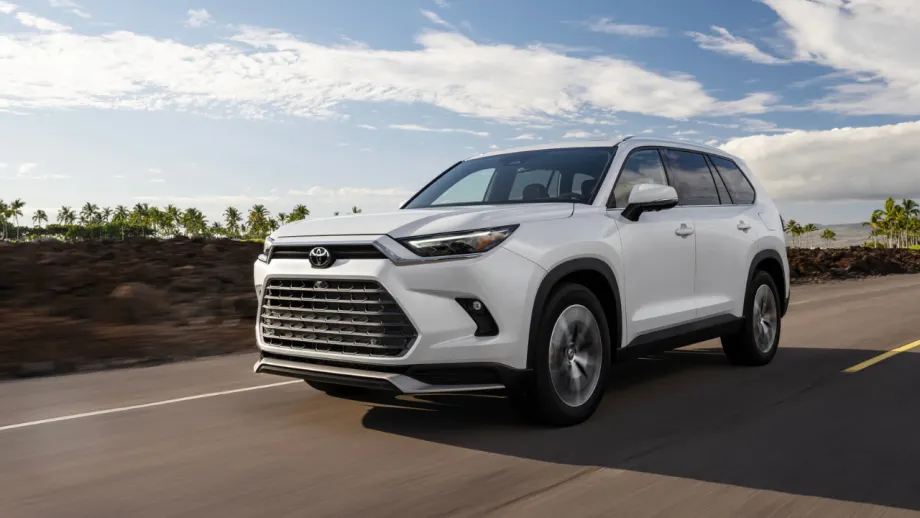 White 2027 Toyota Grand Highlander Limited driving on a paved road with palm trees and blue sky in the background.