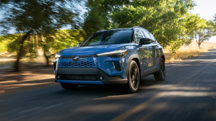 Blue 2027 Toyota Corolla Cross Hybrid XSE AWD driving on a tree-lined road.