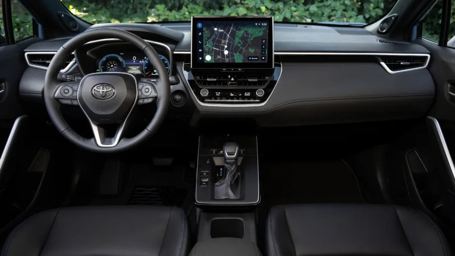 Interior of a 2027 Toyota Corolla Cross Hybrid showing the steering wheel, digital gauge cluster, center touchscreen, and front seats.