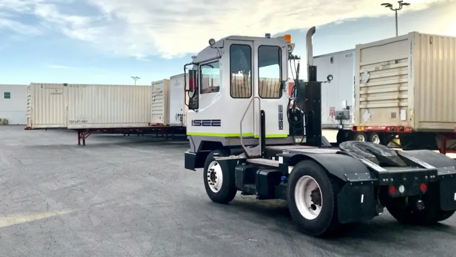 White ISEE autonomous yard truck parked in a shipping yard surrounded by freight trailers and containers.