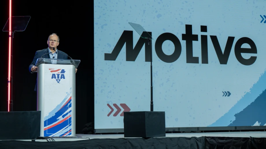 A speaker stands at an American Trucking Associations podium during a conference presentation, with a large Motive logo displayed on the screen behind him.