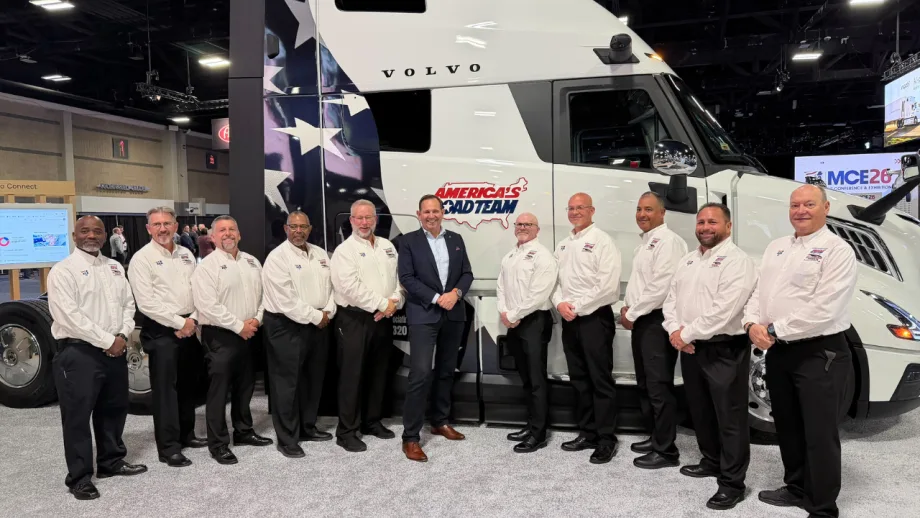 Ten members of the America's Road Team pose in front of a white Volvo semi-truck featuring patriotic graphics and the America's Road Team logo at the MCE26 conference and exhibition.