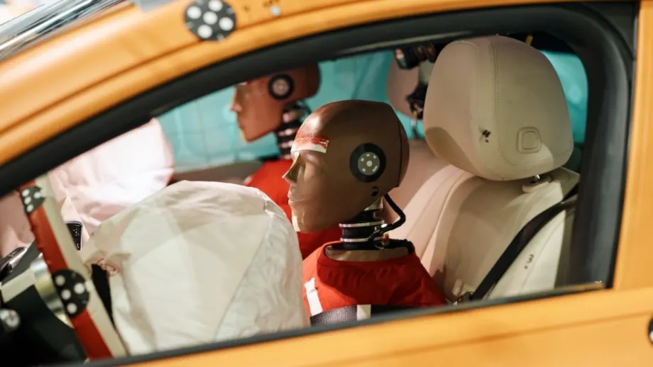 Belted crash-test dummies sit in the front seats of a Mercedes-Benz CLA with airbags deployed after testing.
