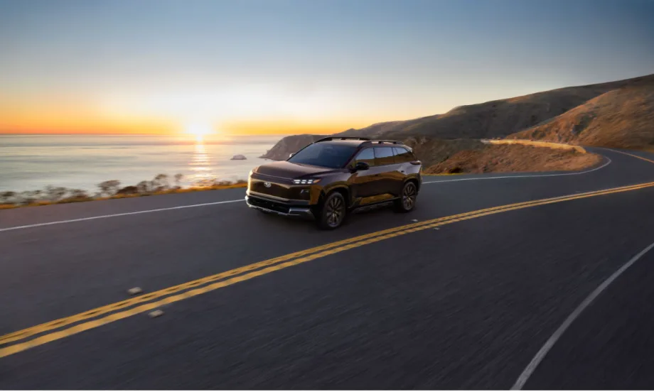 Subaru electric SUV driving along a coastal highway at sunset, representing the 2027 Getaway with three-row seating and all-electric performance.