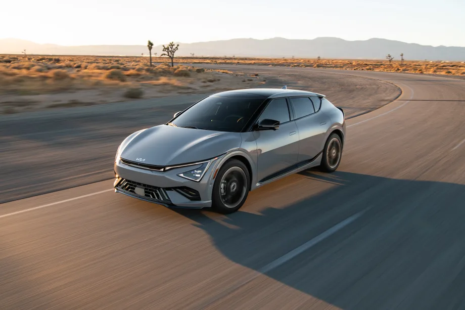 Gray 2026 Kia EV6 electric crossover driving on a desert highway at sunset with mountains and Joshua trees in the background.