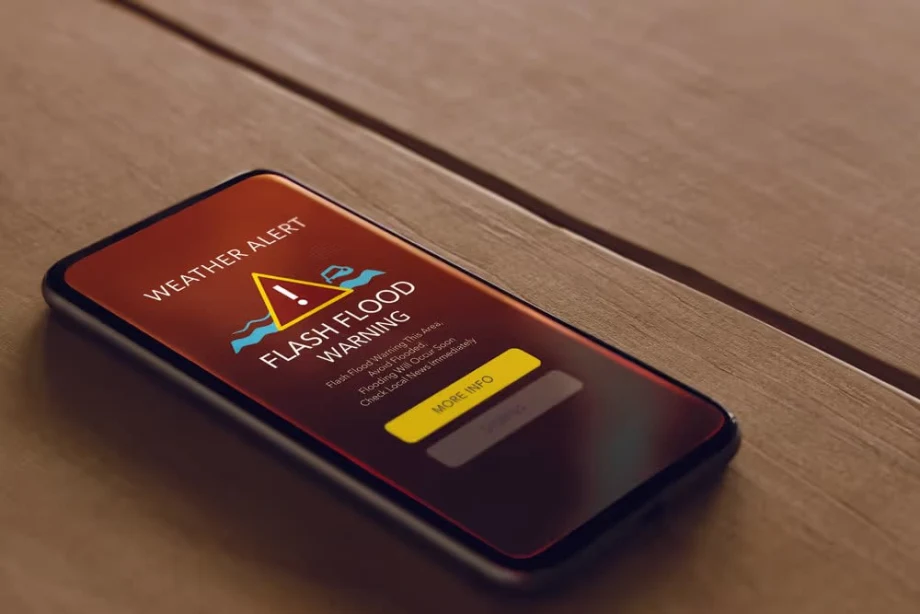 Mobile phone displaying a flash flood weather alert on screen illustrating real-time weather warnings powered by GPS and cloud processing for field safety.