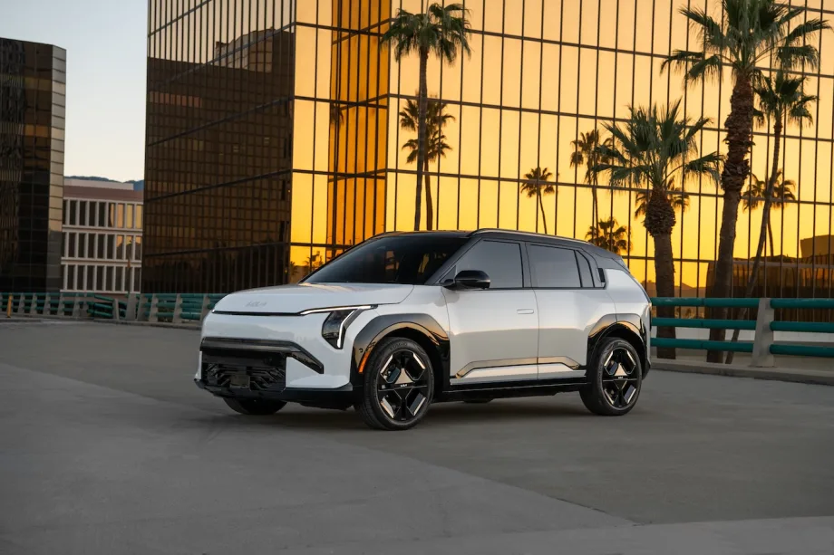 White Kia EV3 electric SUV parked in an urban setting at sunset with palm trees and glass buildings in the background.
