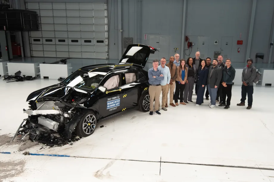 A group of people stand next to a crashed car for IIHS testing