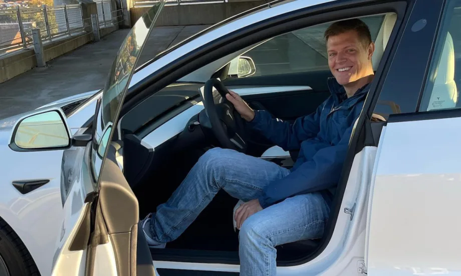 Micah Bergdale sits turned sideways in the driver's seat of a Tesla with the door open.