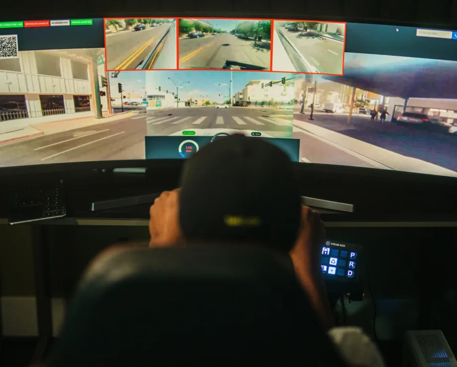 Back view of a remote driver in front of a screen delivering a car to a location.