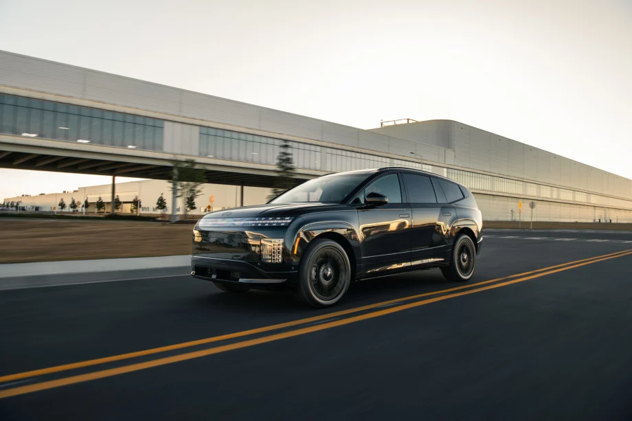 Black Hyundai IONIQ 9 electric SUV driving on a road near a modern industrial building.