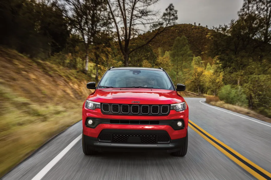 A red 2027 jeep compass drives on the road surrounded by foliage