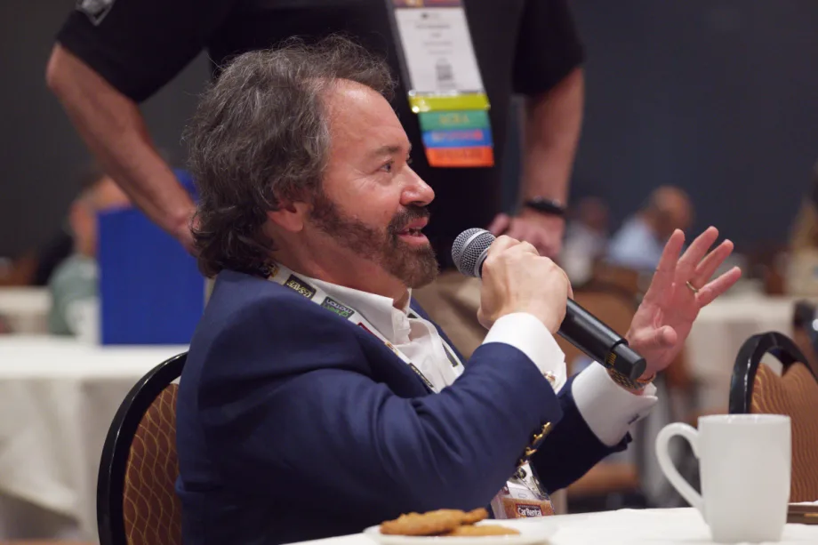 John Possumato holding microphone while asking a question during a live conference session at the ICRS Show.