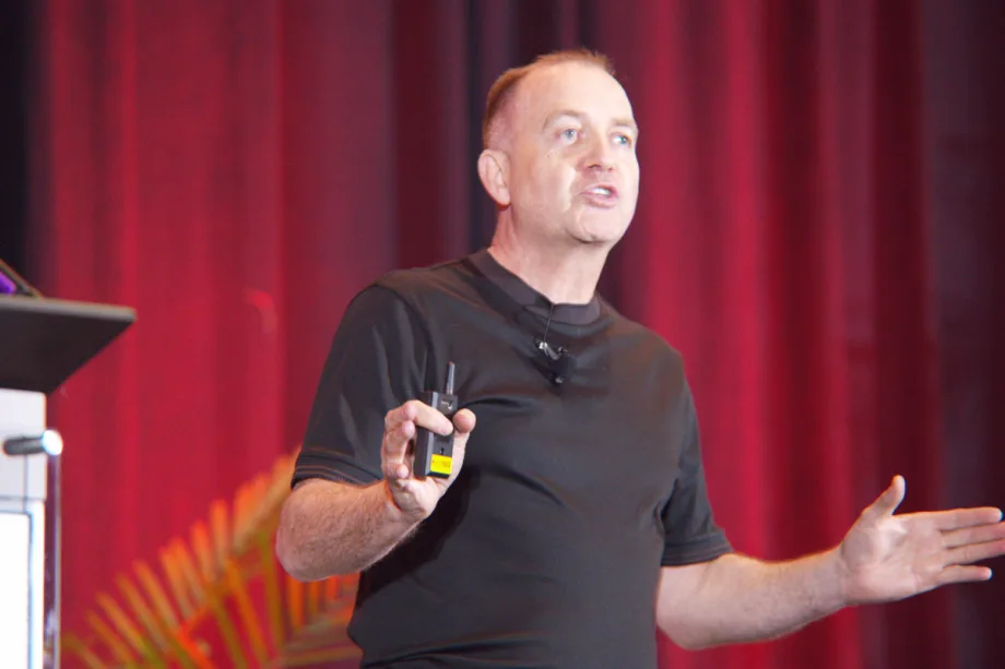 Richard Lowden gesturing on stage in front of a red curtain at the Gaylord Texan Resort near Dallas.