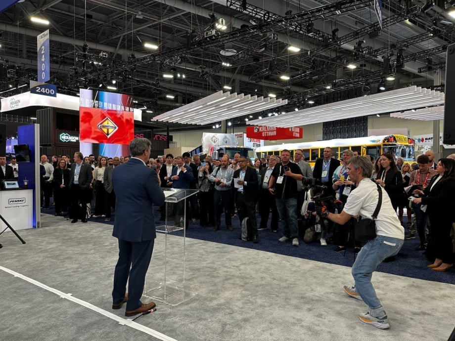 Man standing at podium in expo hall in front of reporters and industry representatives.