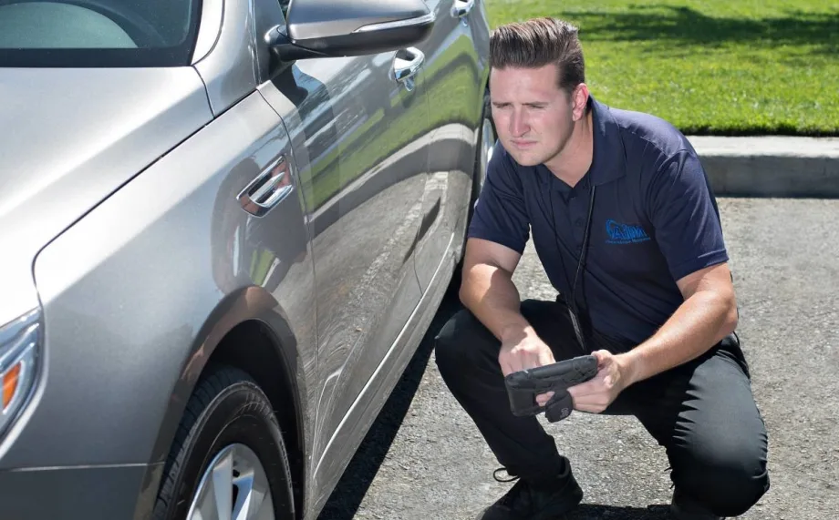 An inspector with a tablet looks at the left side of a gray vehicle.
