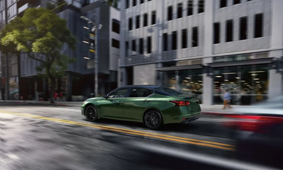 The 2026 Nissan Altima drives on a road between white buildings.