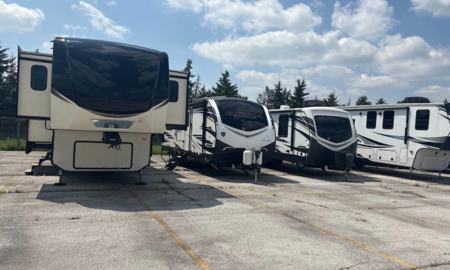 Camper trailers lined up in a parking lot underneath a blue sky with white puffy clouds.