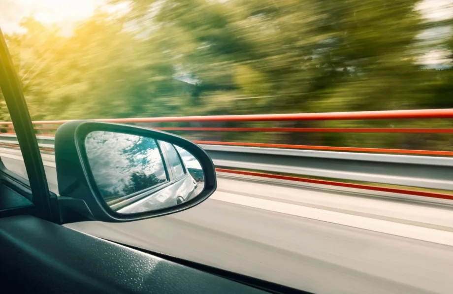 Image of a bridge and trees rushing by from inside of a moving car.