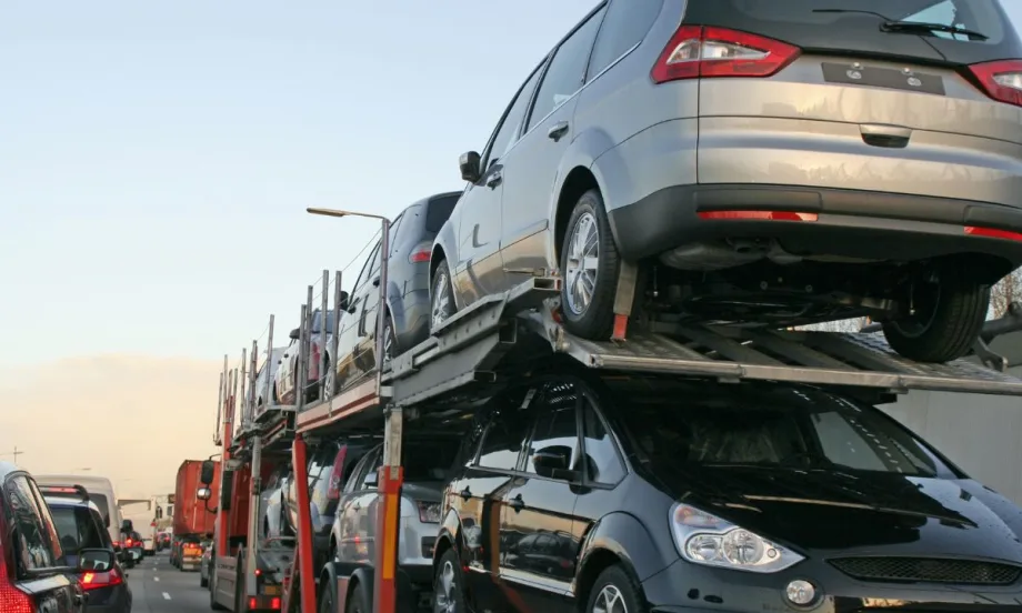 A double-decker stinger transport trailer loaded with cars drives down a crowded freeway.