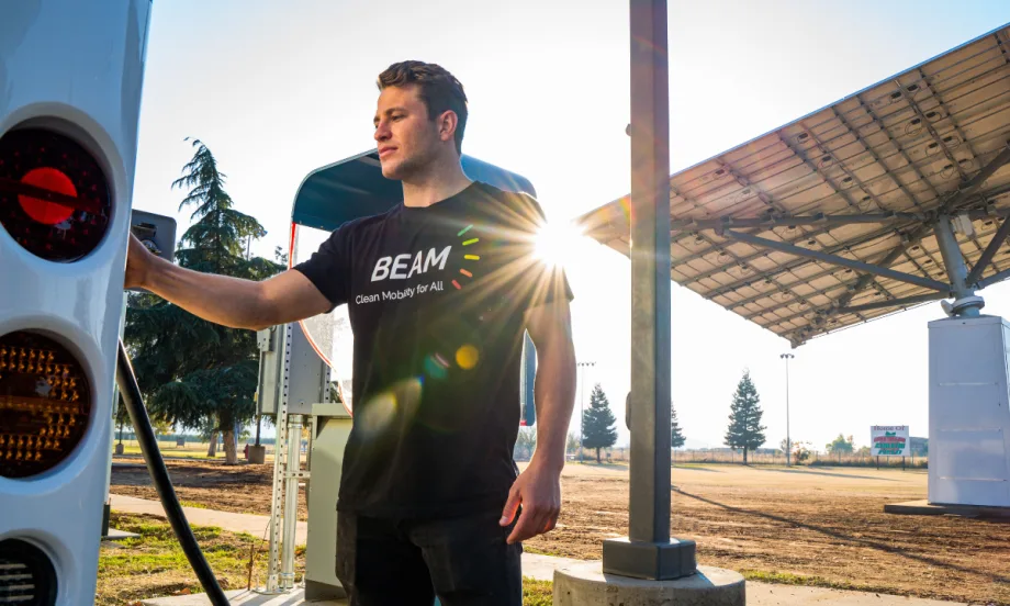 A person uses a Beam Global EV ARC off-grid EV charger next to a solar panel canopy.
