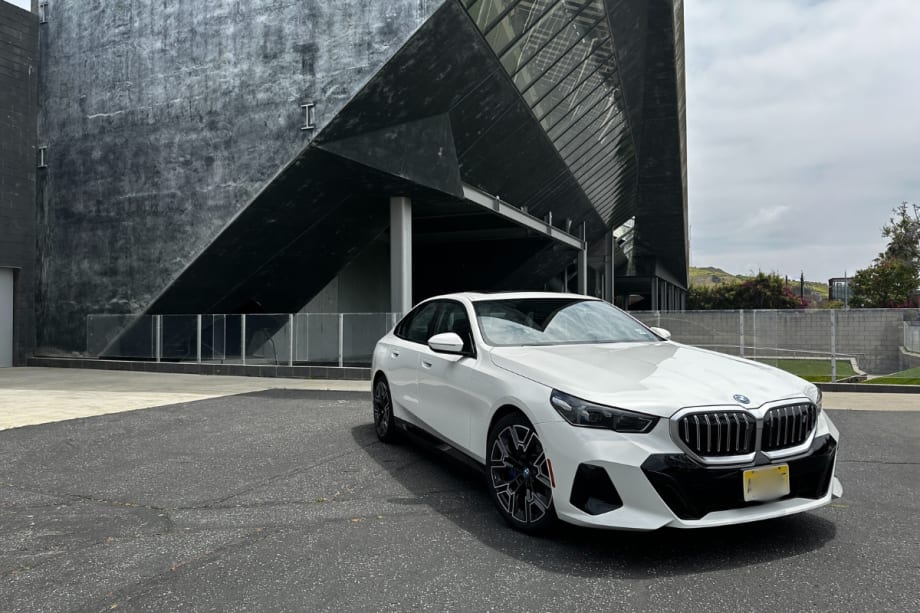 A three-quarter of a white sedan with a modern building in the background.