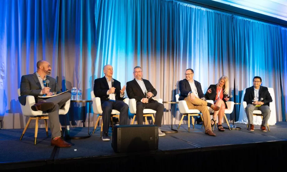 Six panelists on a stage in front of a blue curtain.