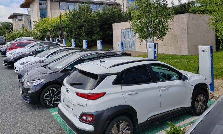 A front view of a row of electric vehicles lined up at parking lot chargers.