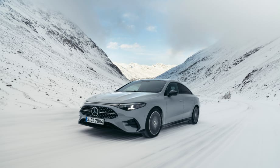 A metallic white hybrid Mercedes-Benz CLA drives between two snowy mountains.